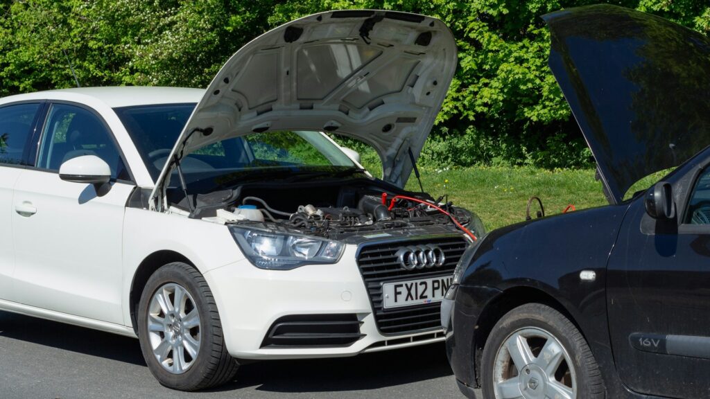 Auto met open motorkap krijgt hulp van andere auto met startkabels tijdens pech onderweg op een rustige weg