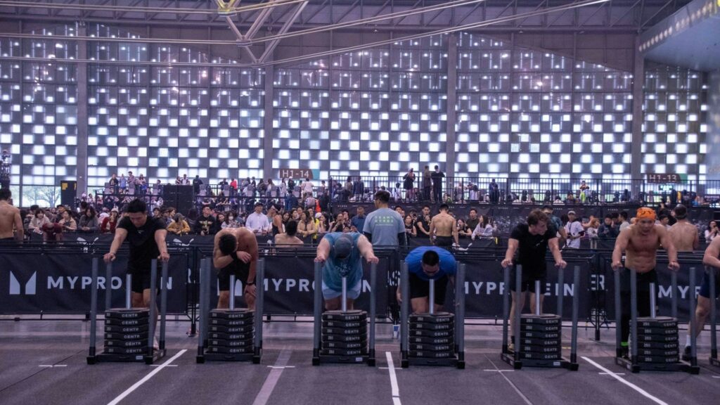 Groep deelnemers duwt sleds tijdens een HYROX event met publiek, illustratie van waarom HYROX groeit snel in populariteit