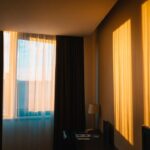 Donkere gordijnen met witte vitrage voor het raam in een minimalistisch ingerichte kamer met warm avondlicht